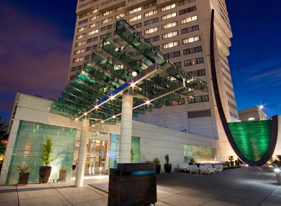 The glass canopy entrance of Hotel Murano in Tacoma at dusk, lit from below with a green water feature alongside.
