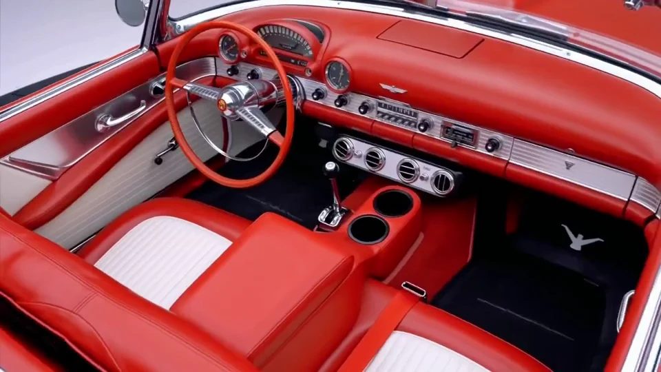 Red and white interior of the 1955 Ford Thunderbird showing the steering wheel, dashboard gauges and bench seat.