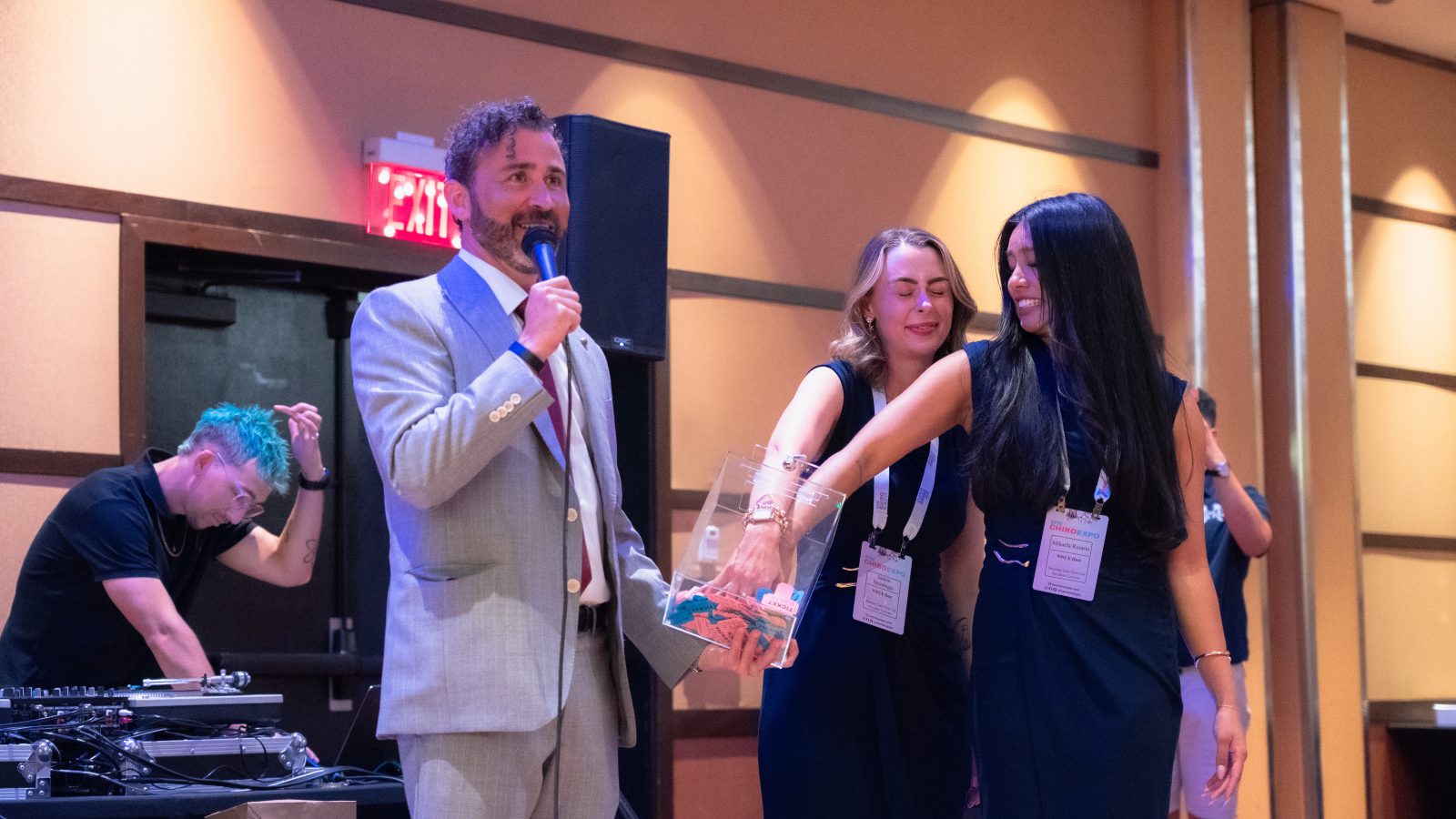 Josh Brumley on the microphone as two NW Chiro Expo team members draw the winning ticket from a clear box.