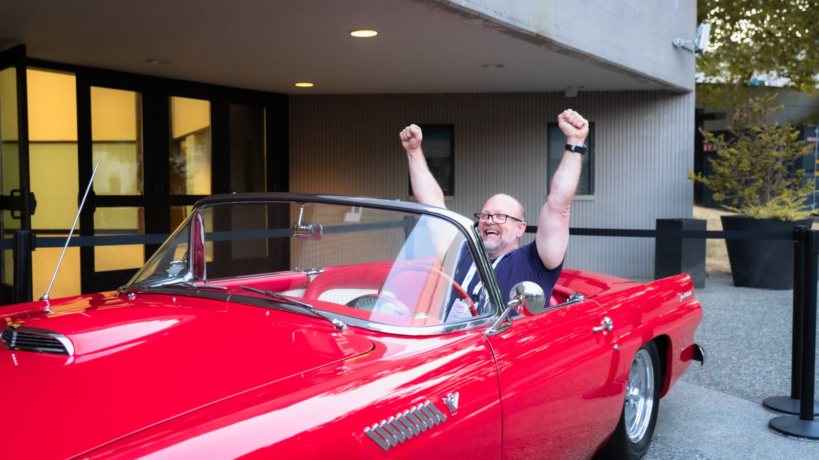 The winner raises both fists in celebration from the driver's seat of the red Thunderbird.